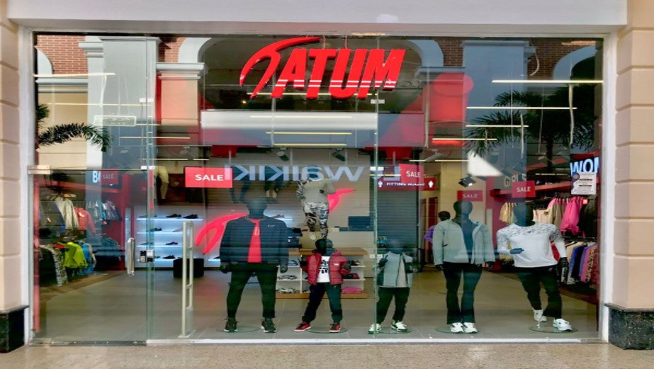 a group of people standing in front of a store window with a red and white sign that says Atum 